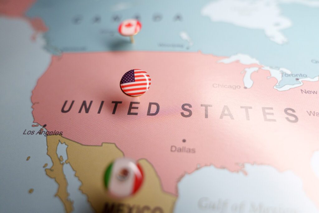 US flag push pin marking the United States on a map, with Mexico and Canada location pins visible. High quality photo