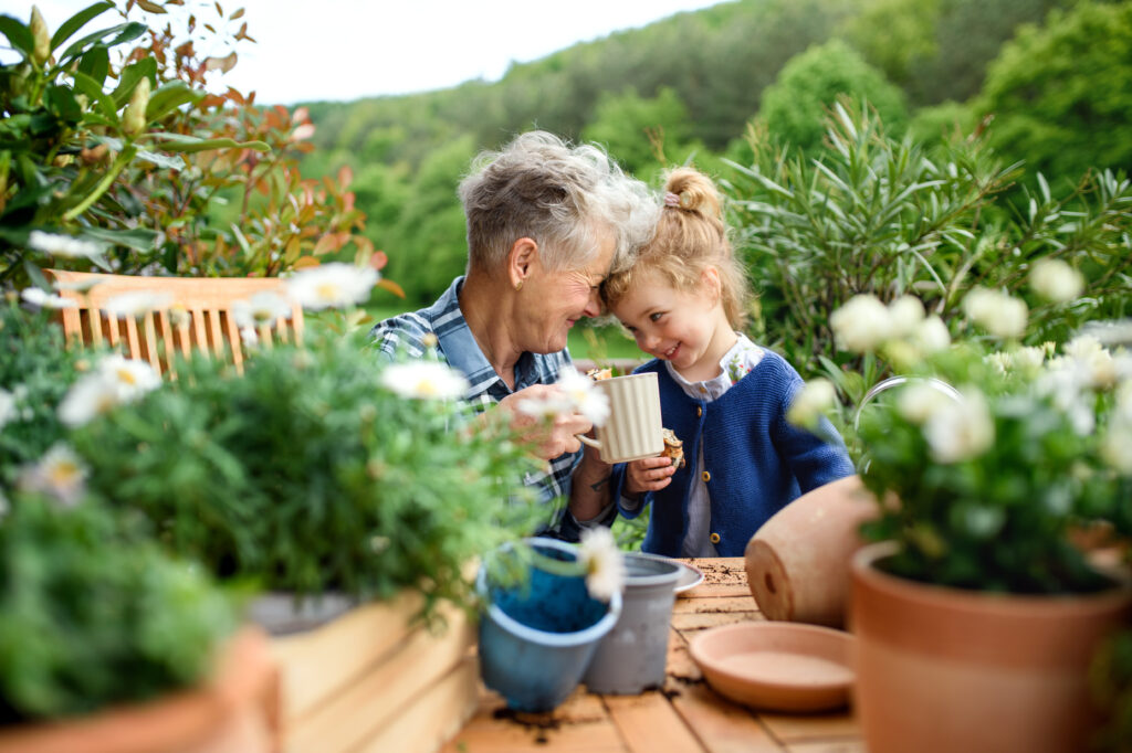 Happy senior grandmother with small granddaughter gardening on balcony in summer, resting.