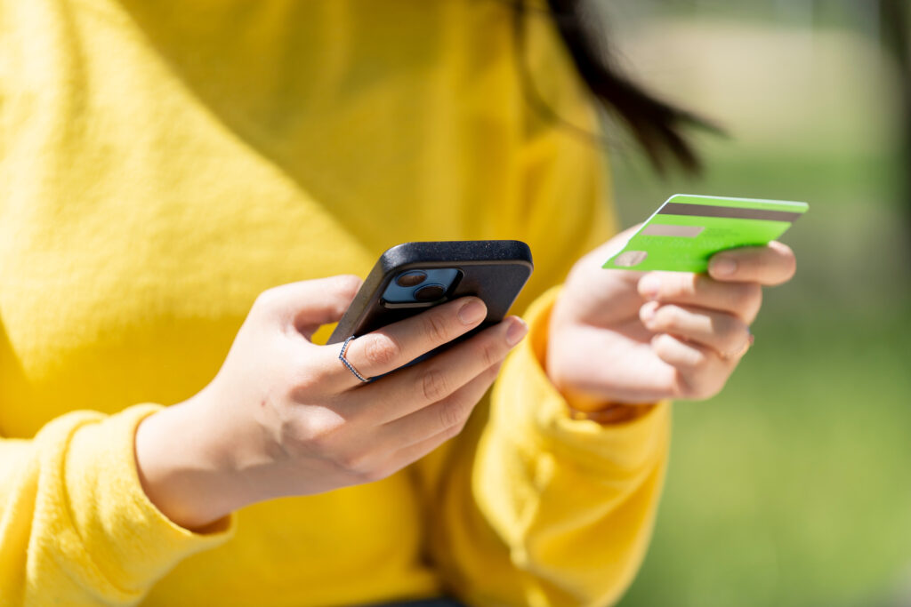 A woman with smart phone buying with credit card online in the park