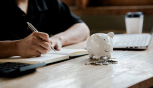 Person budgeting with notebook and piggy bank on desk