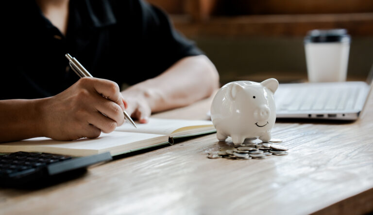 Person budgeting with notebook and piggy bank on desk
