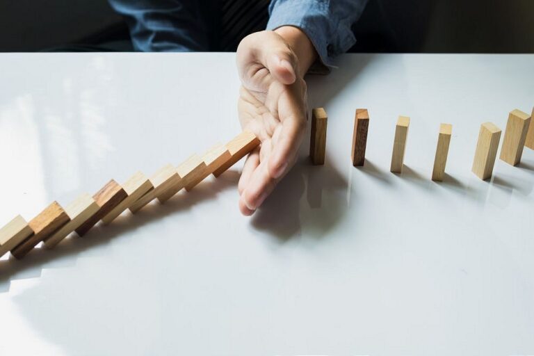 Hand stopping falling wooden dominoes on white table