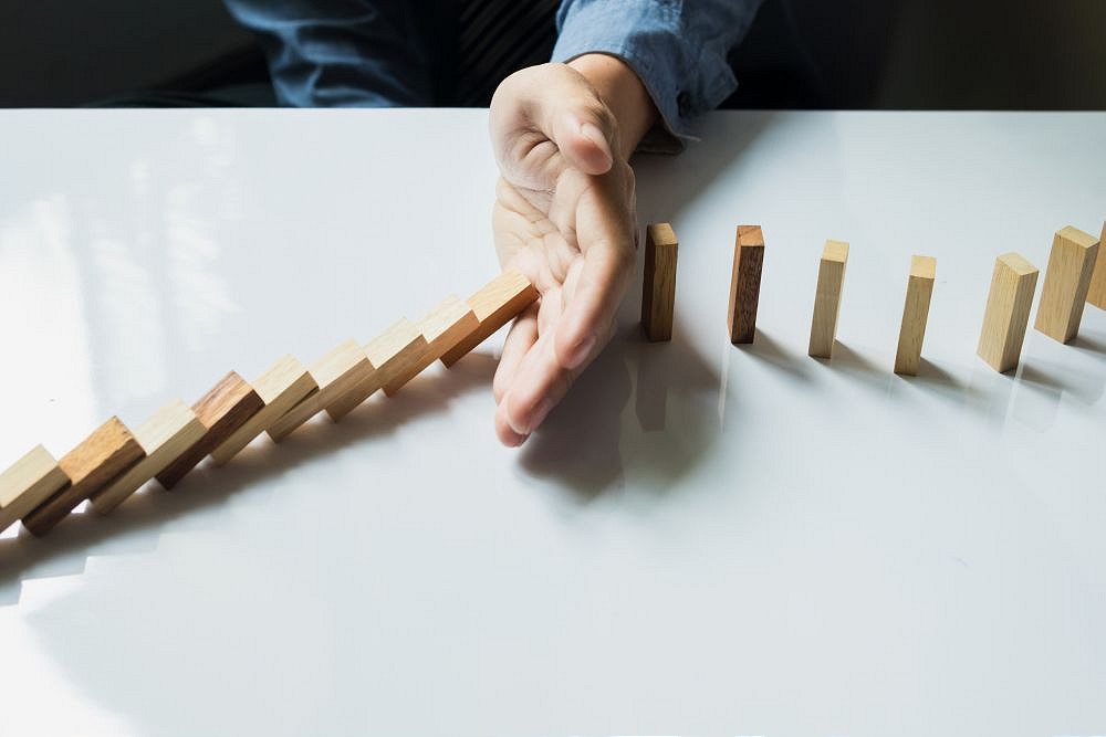 Hand stopping falling wooden dominoes on white table